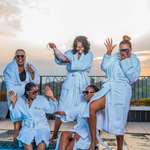 Five women in robes sitting by a pool with a scenic background